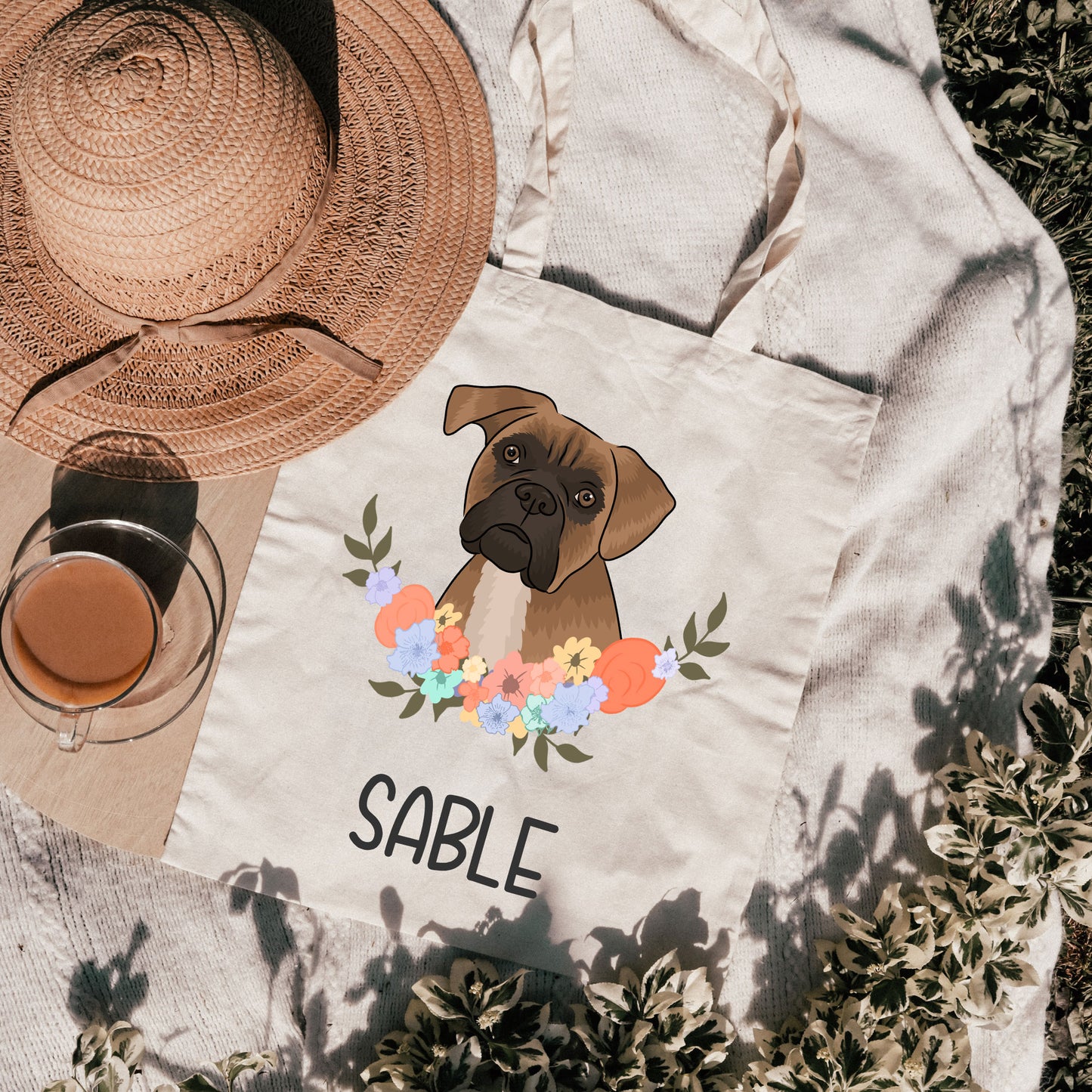 A personalised tote bag with an illustration of a dog, specifically a Boxer, surrounded by a floral pattern on a beige background. The text 'SABLE' is also visible on the bag.
