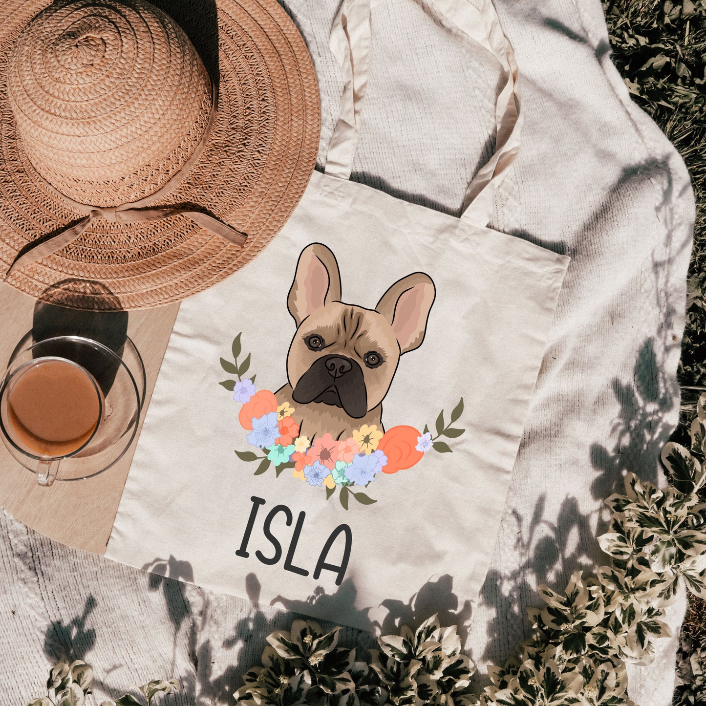 A beige tote bag with a printed French Bulldog design and the text 'ISLA' on the front, alongside a floral wreath.