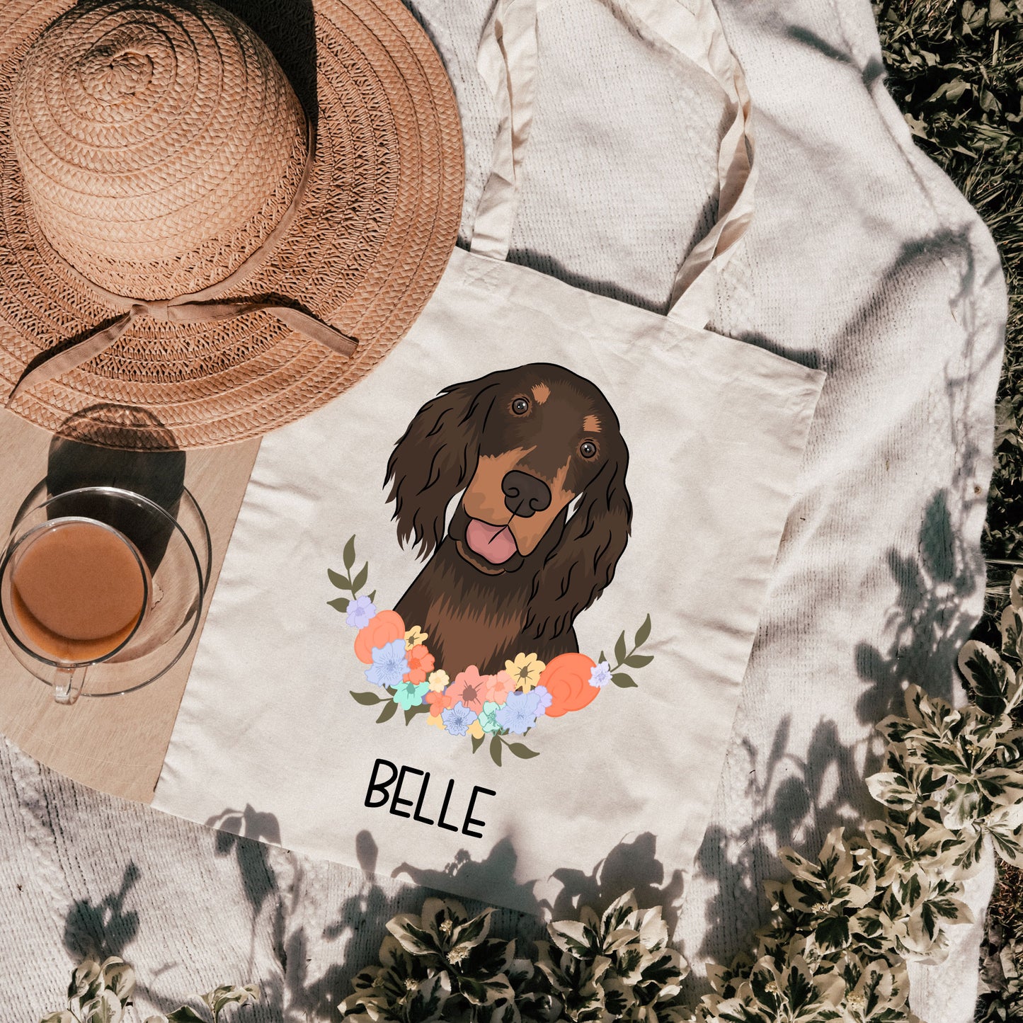 A canvas tote bag with an illustration of a brown dog, likely a Gordon Setter, surrounded by a floral wreath with the name 'Belle' printed on it.