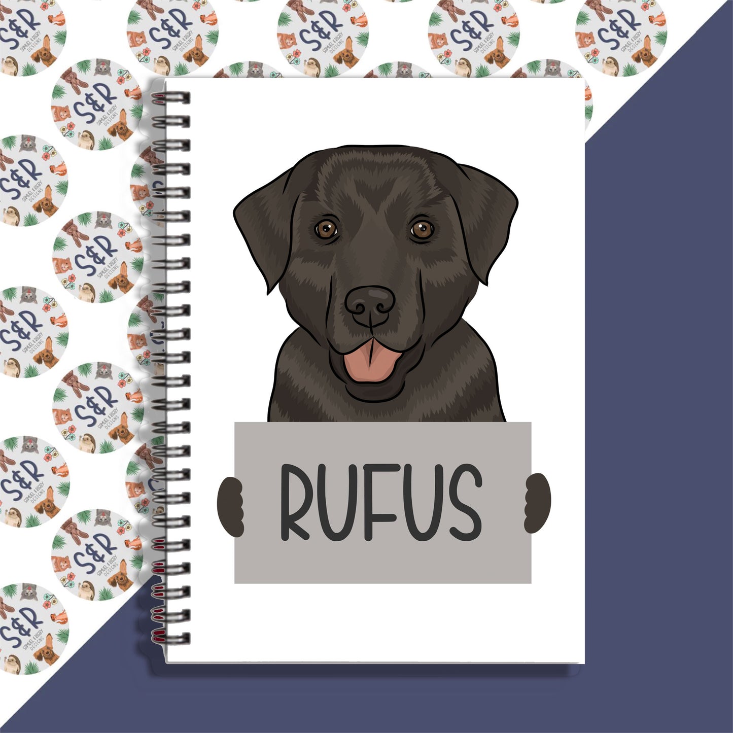 A notebook with a spiral binding featuring a graphic of a black Labrador dog on the front cover, with the name 'Rufus' written on the cover.