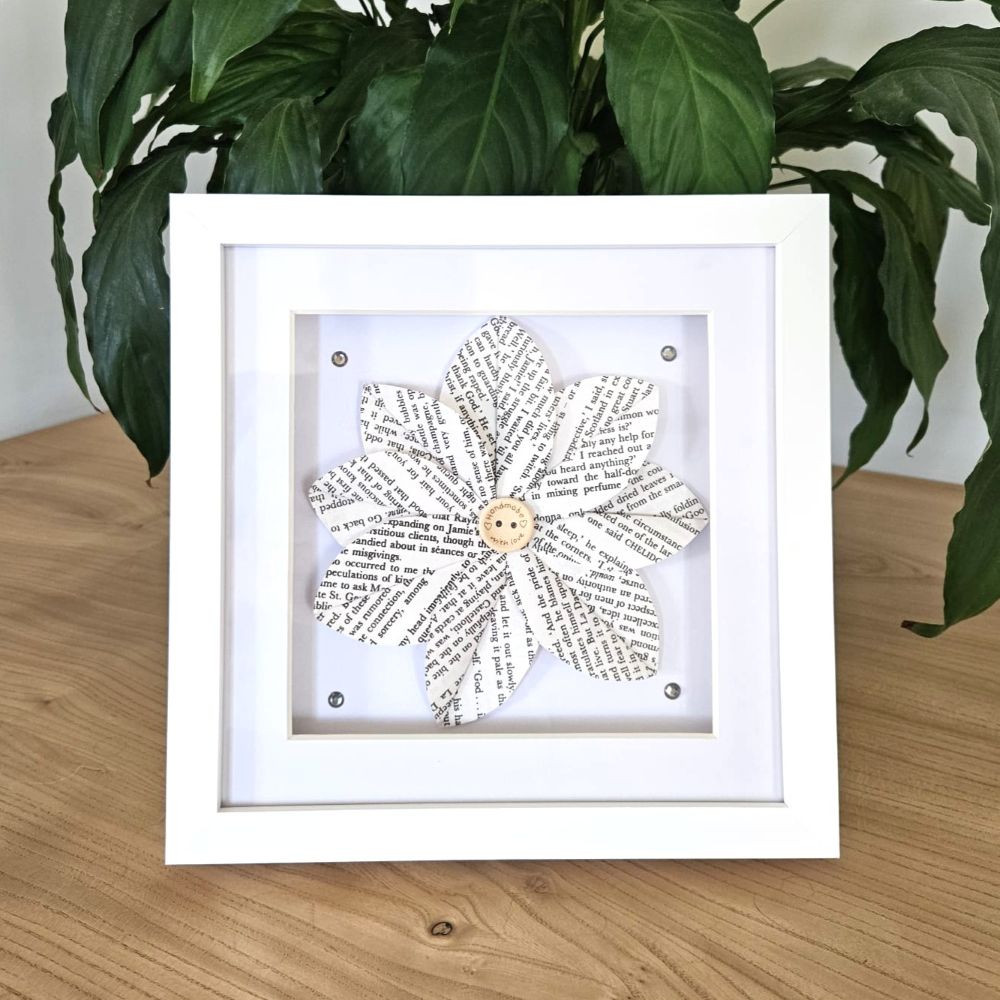 Framed decorative item with a floral design on a wooden surface with a plant in the background