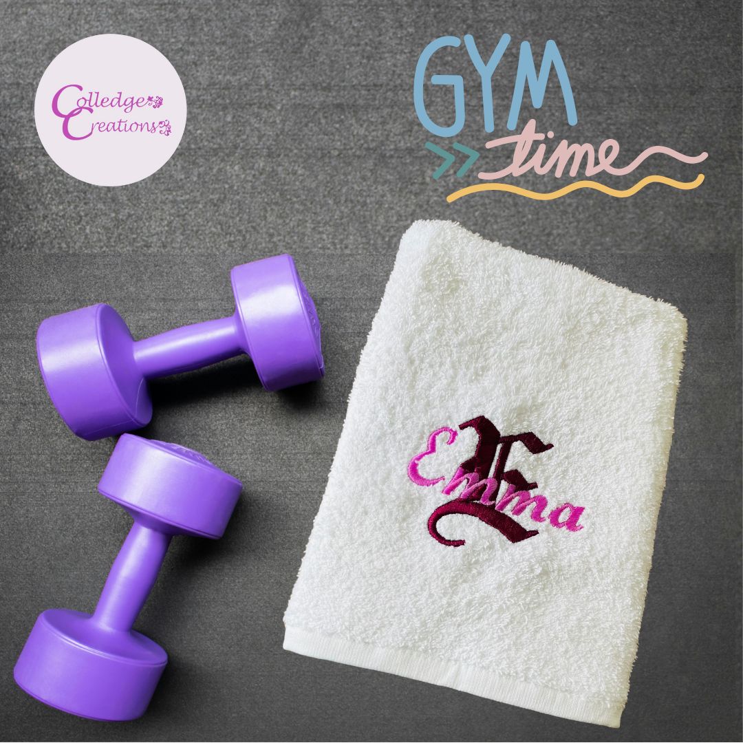 White towel with 'Emma' embroidery, purple dumbbells, and 'Gym Time' text on a grey background.