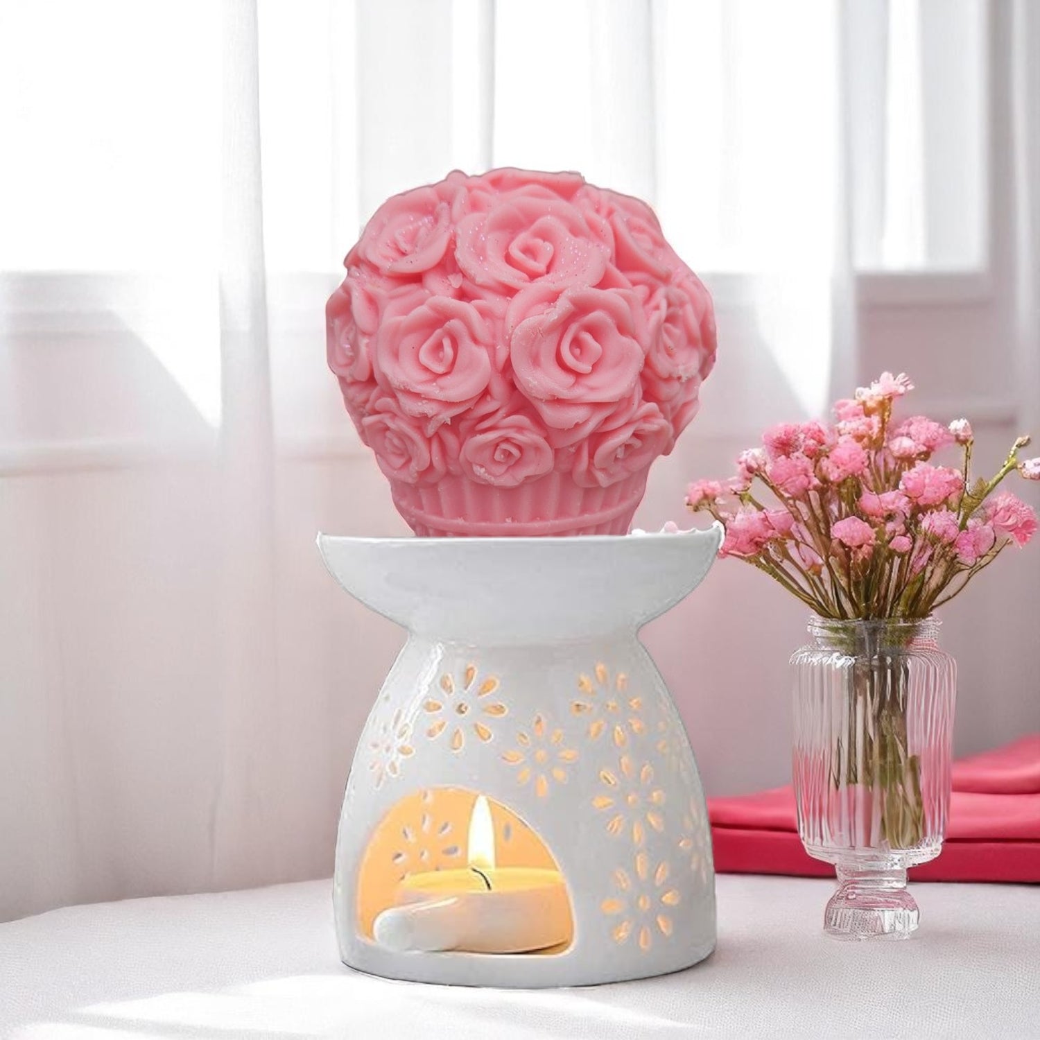 Pink rose design wax melt with a lit candle and a vase of pink flowers on a white surface.
