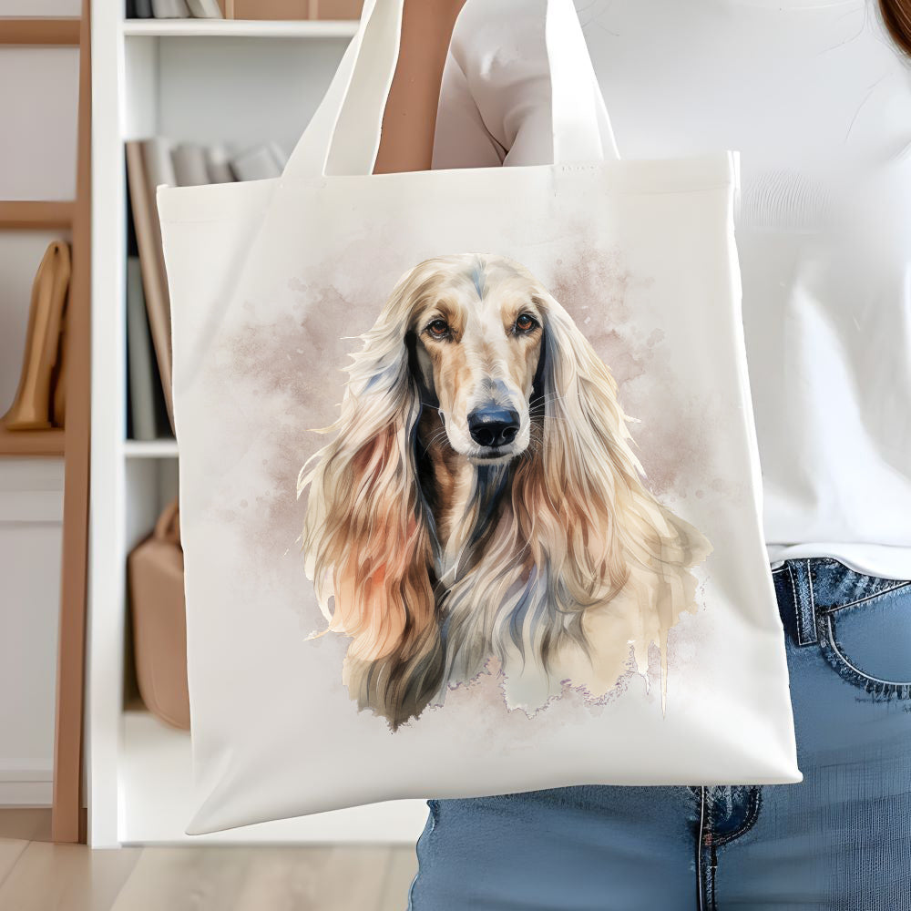 White long handled tote bag showing an Afghan Hound head shot and long flowing hair facing forward. A smoky brown background decorates. A woman is holding the bag  in front of white book case.