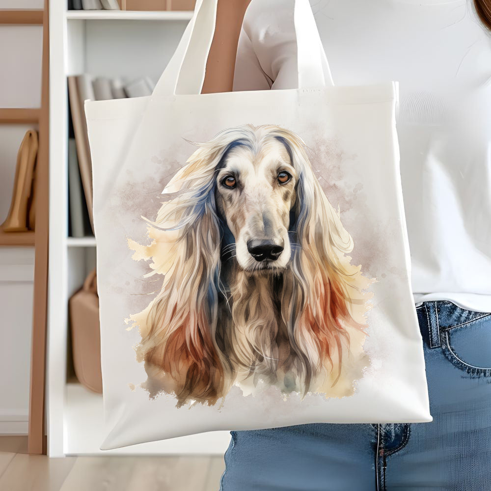 White long handled tote bag showing an Afghan Hound head shot facing forward. A smoky brown background decorates. A woman is holding the bag  in front of white book case.