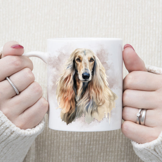 A white ceramic mug with a head image of an Afghan Hound with long flowing hair. A grey/brown smoke effect decorates the background. A woman is holding the mug in two hands.