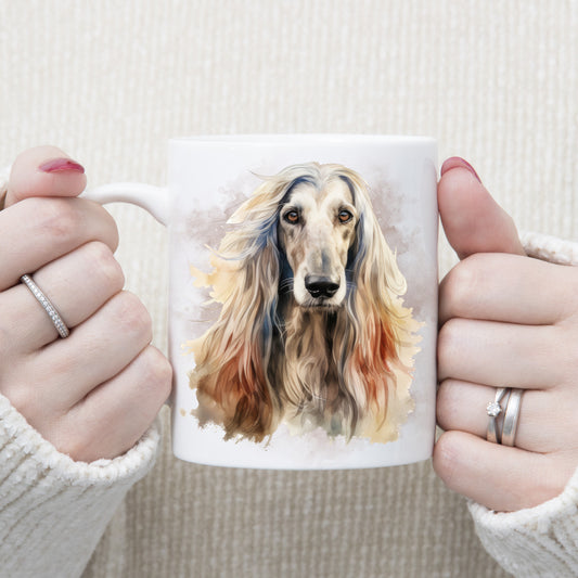A white ceramic mug with a head image of an Afghan Hound with long flowing hair. A grey/brown smoke effect decorates the background. A woman wearing rings is holding the mug in two hands.