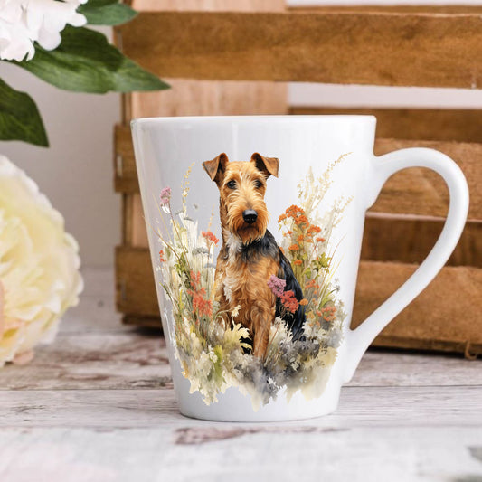 A 12oz ceramic latte mug with a printed image of an Airedale Terrier dog, surrounded by floral elements and a wooden crate in the background.