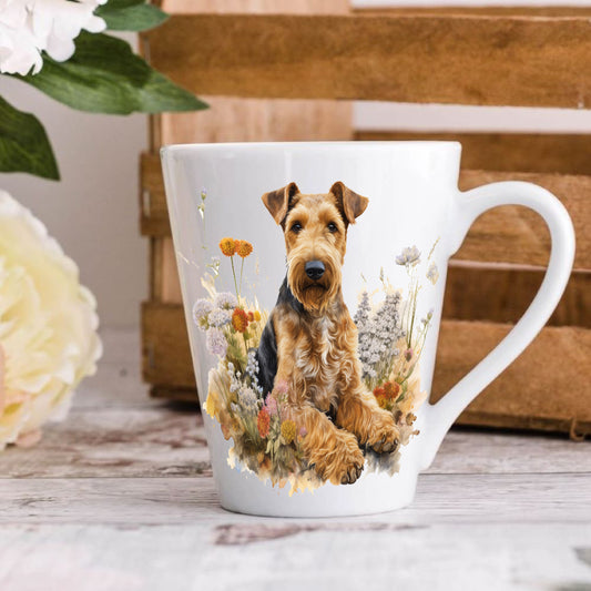 A ceramic latte mug with a printed image of an Airedale Terrier dog, surrounded by floral elements and a wooden background.