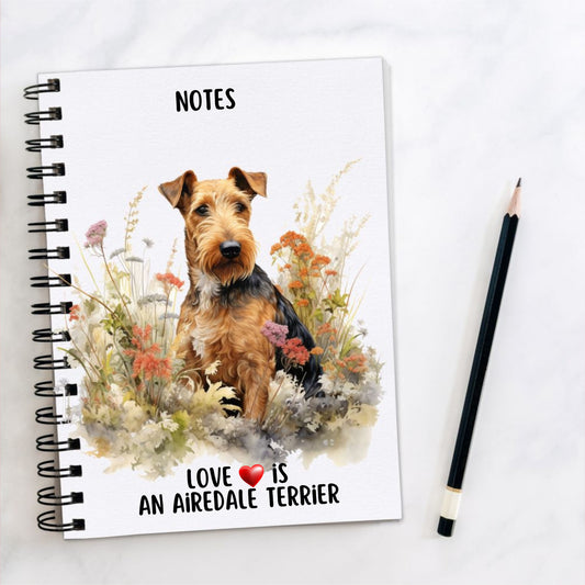 White spiral bound notebook with an Airedale Terrier gazing right sat among wildflowers on the front and a quote written at the bottom. A black pencil is placed to the right hand side.