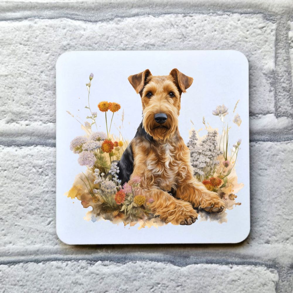 White drinks coaster placed on a grey, brick effect surface. The coaster shows a  an Airedale Terrier laid among flowers.  