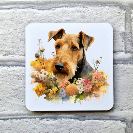 White drinks coaster with a head shot of an Airedale Terrier. Multi-colour flowers decorate. The coaster is placed on a grey, brick effect surface.