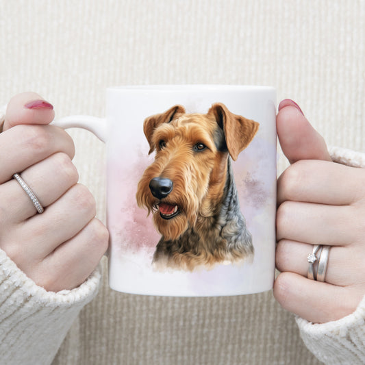 A head shot of an Airedale Terrier dog in front of a smoky background on a white ceramic mug. A woman is holding the mug with both hands.