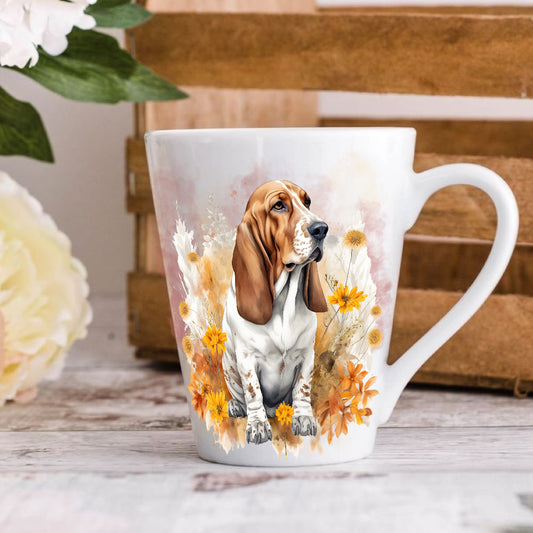 A latte coffee mug with a colorful illustration of a Basset Hound dog surrounded by flowers, displayed on a wooden table.