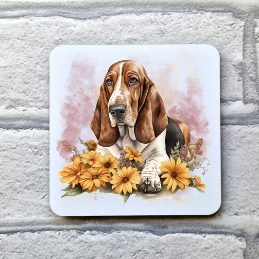 A White table coaster with a Tri-coloured Basset Hound laid among orange flowers. The coaster is placed on a grey, brick effect surface.