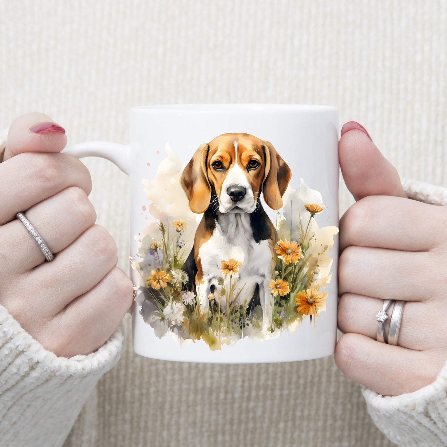 A Beagle dog sits among orange and white flowers on a white ceramic mug which is being held by a woman.