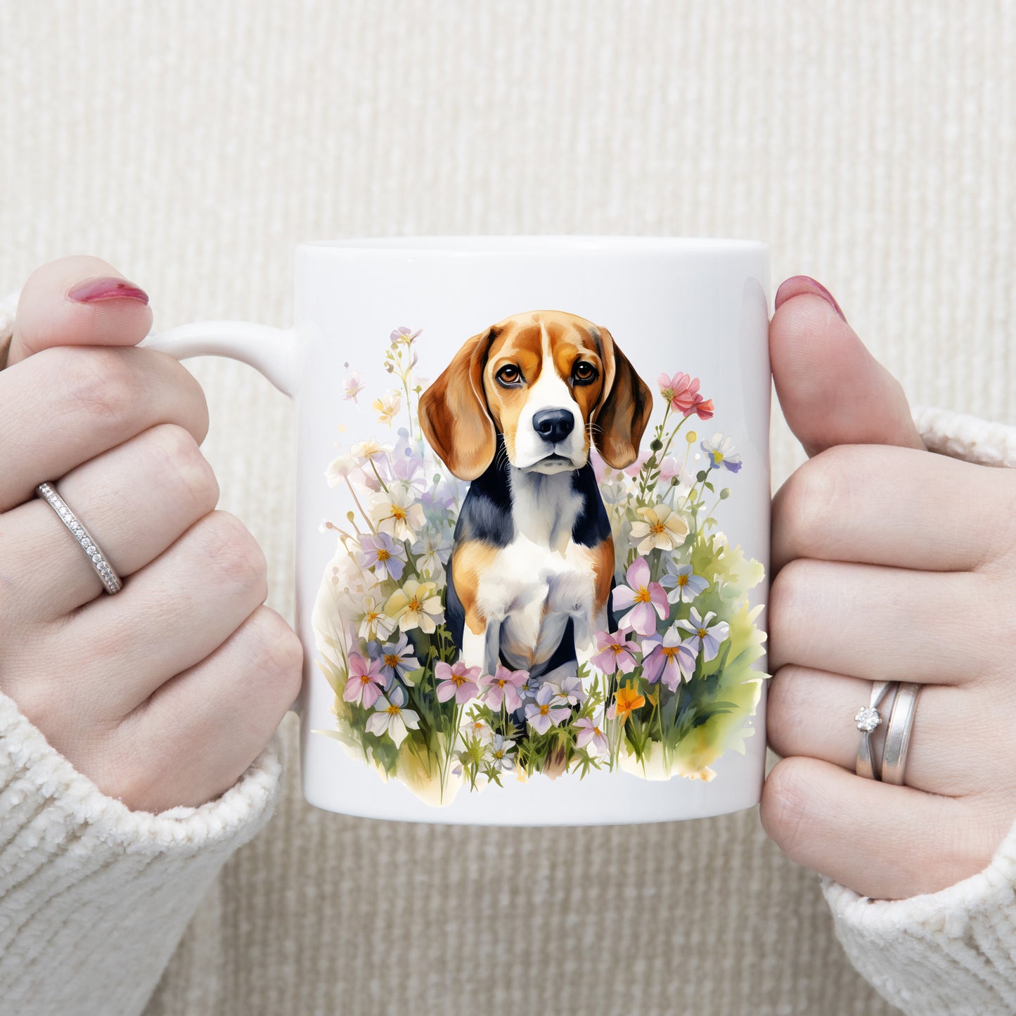 A watercolour image of a Tri-coloured Beagle dog with a white chest sitting among pink and purple wildflowers.  A woman is holding the mug in two hands.