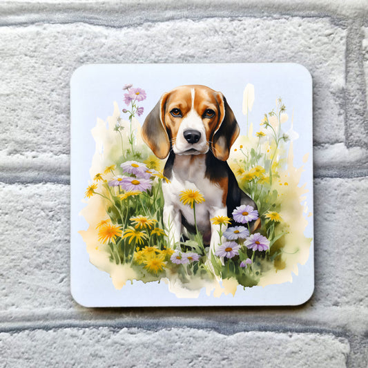 A Beagle sitting among purple and orange flowers, looking forward with a soft expression. This image is on a white coaster. The coaster is placed on a grey, brick effect surface.