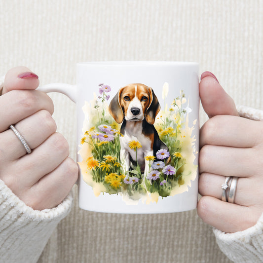 A Beagle dog is sat among purple and yellow wildflowers on a white ceramic mug. A woman is holding the mug with both hands.