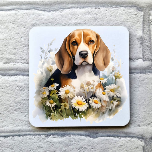A Beagle pup is sat among daisies looking forward with a soft expression. This image is on a white coaster. The coaster is placed on a grey, brick effect surface.