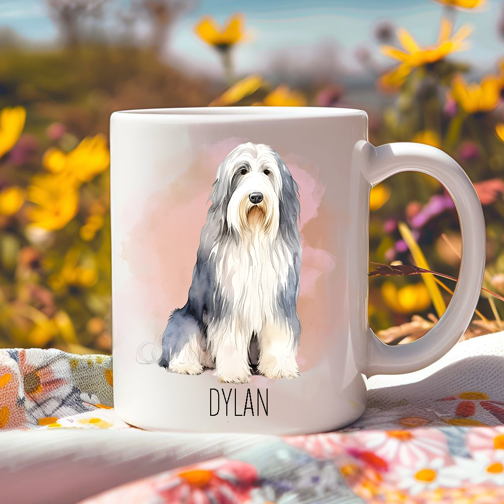 Bright yellow flowers surround this lovely personalised ceramic mug depicting a seated Bearded Collie.  The mug is placed on a floral multi-coloured tablecloth.