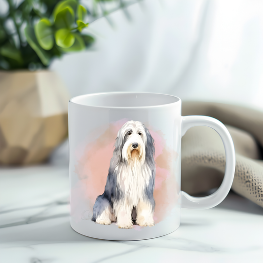 Bearded Collie in a sitting position on a white ceramic mug which has been placed on a grey marble surface.  A plant decorates the left corner.