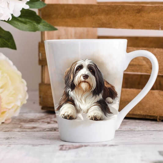 A white ceramic latte mug stands on a wooden surface with a crate in the background. The mug features a Bearded Collie.  A large yellow flower peeps in from the left hand side.