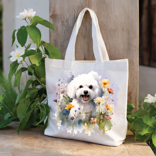 White Tote Bag featuring a vibrant printed image of a Bichon Frise dog sat among various flowers and with a lilac smokey background. The Tote Bag has been placed on a wooden surface. Plants with white flowers decorate both sides.