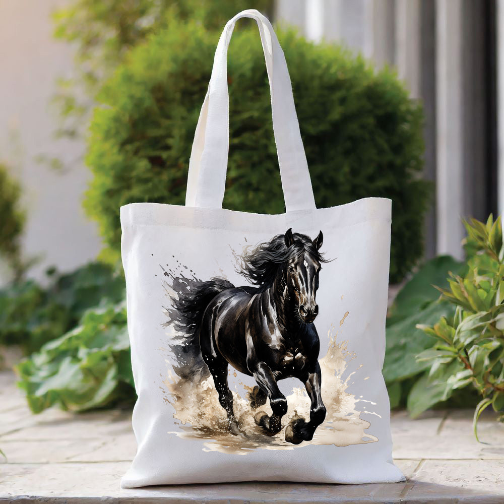 White tote bag with a long handle showing a black horse running through water.  The bag is placed in front of a large green shrub with green foliage to the right side.