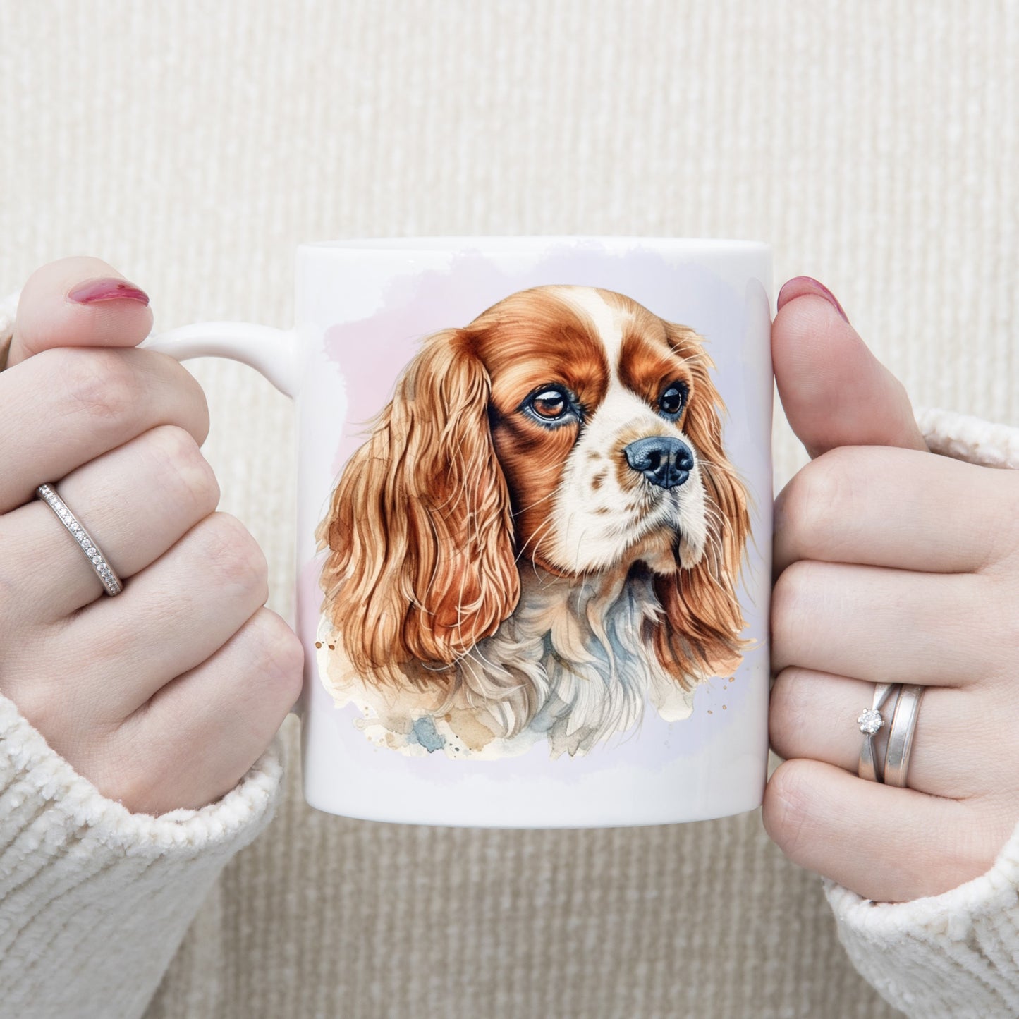 A headshot of a Blenheim Cavalier King Charles Spaniel dog facing right.  A woman is holding the mug in two hands.