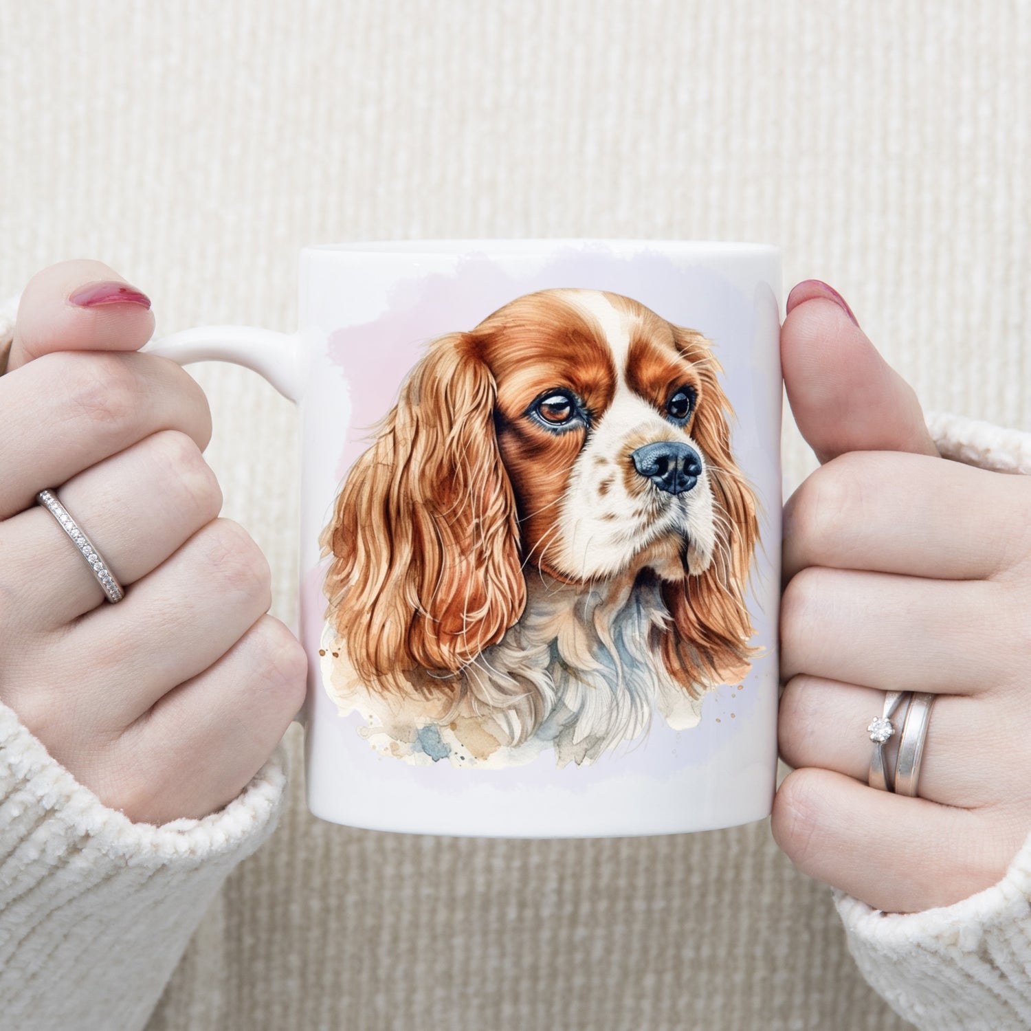 A headshot of a Blenheim Cavalier King Charles Spaniel dog facing right.  A woman is holding the mug in two hands.