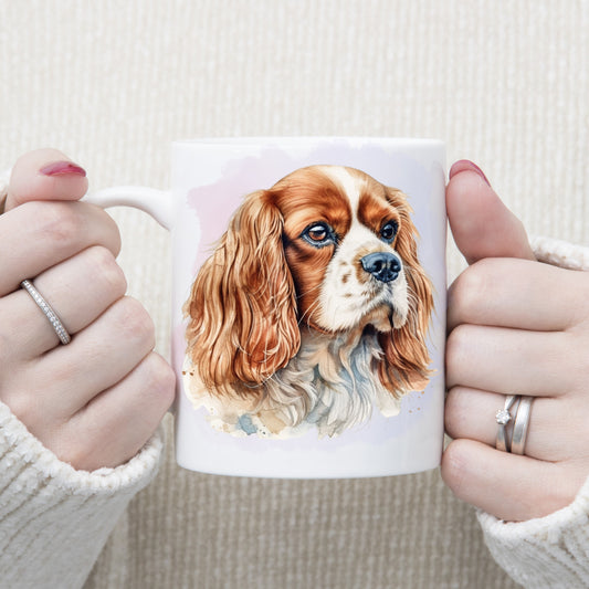 A headshot of a Blenheim Cavalier King Charles Spaniel dog facing right.  A woman is holding the mug in two hands.