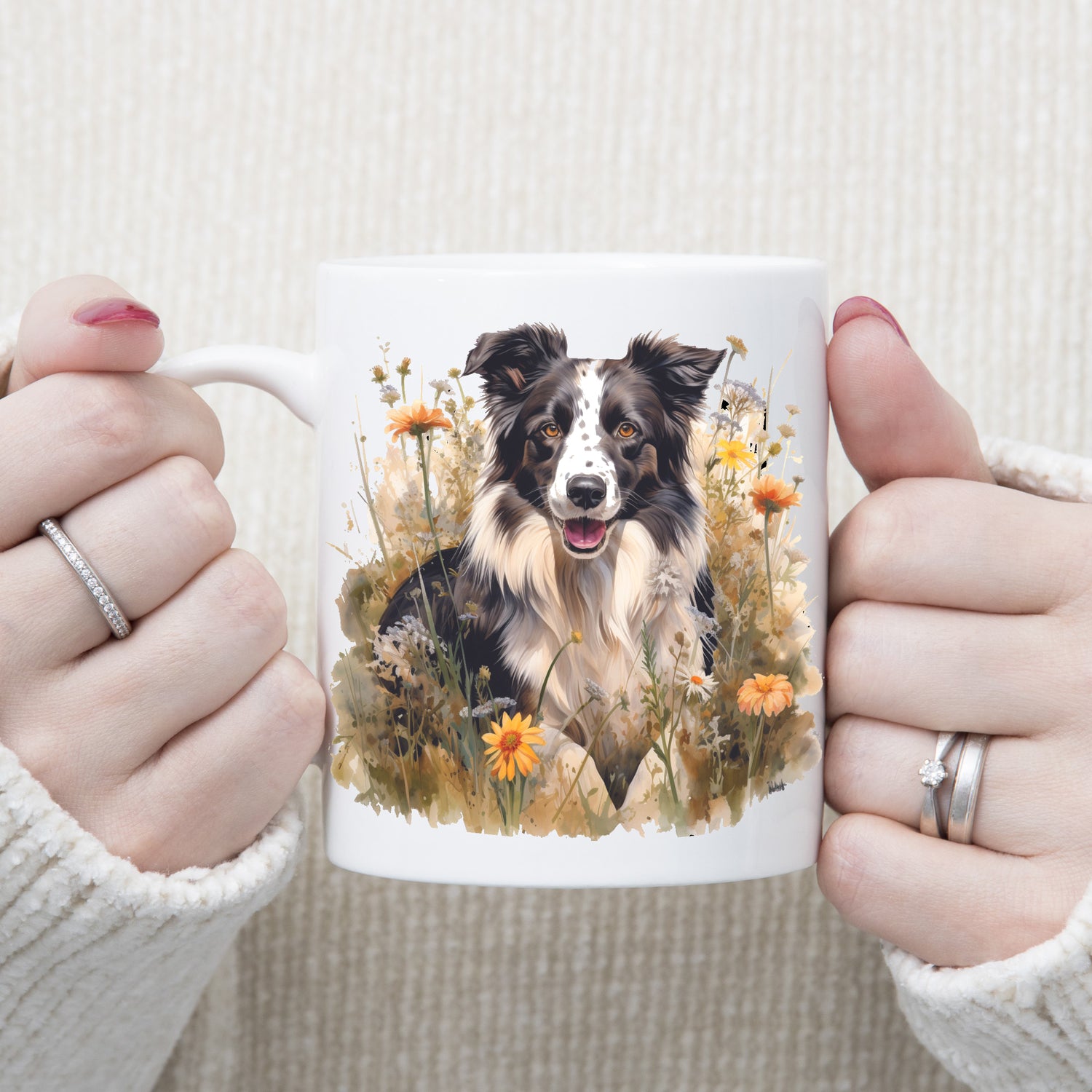 A white ceramic mug with a black and white Border collie sat among grass and orange flowers. The mug is being held by a woman.