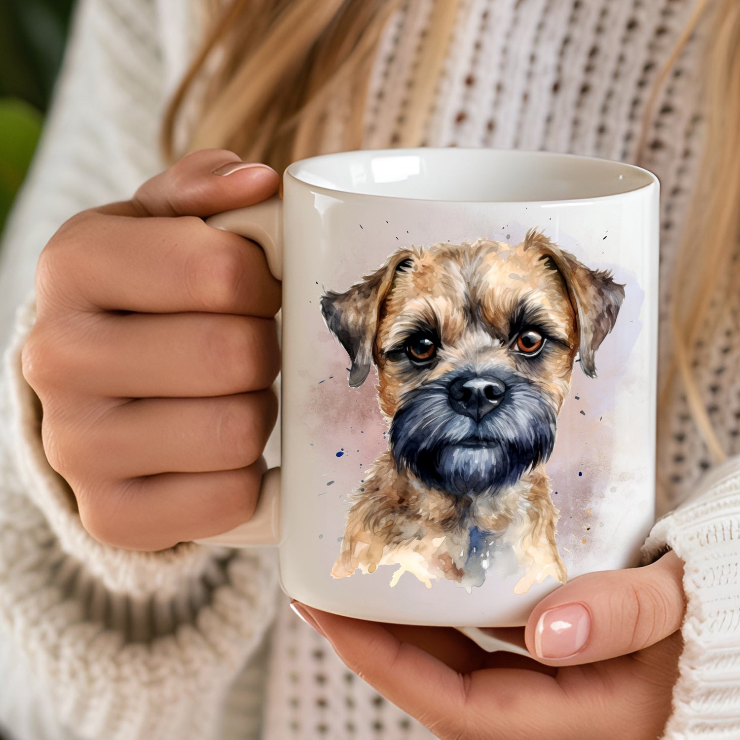 White 11oz ceramic mug has a vibrant printed image of a Border Terrier dog head shot with a smokey background.  The mug is being held in a woman's hands.