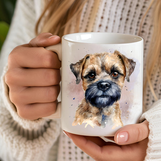 White 11oz ceramic mug has a vibrant printed image of a Border Terrier dog head shot with a smokey background.  The mug is being held in a woman's hands.