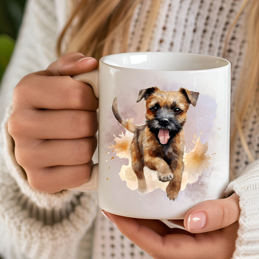 White 11oz ceramic mug has a vibrant printed image of a Border Terrier dog running with a smokey background.  The mug is being held in a woman's hands.