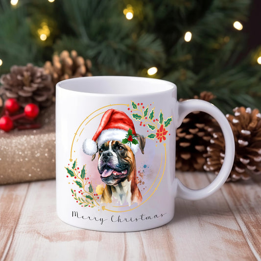 Boxer dog wearing a Santa hat on a white ceramic Christmas themed mug positioned on a wooden surface in front of a Christmas tree and gifts.
