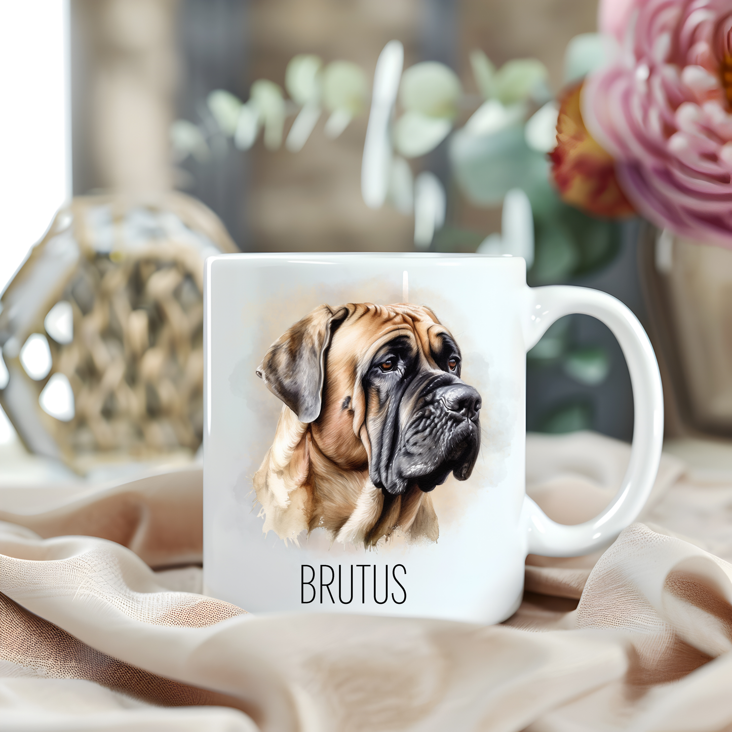 A Bullmastiff headshot looking to its left is placed on a white personalised ceramic mug.  The mug sits on a beige cloth with a large pink flower and green foliage accessorizing the background