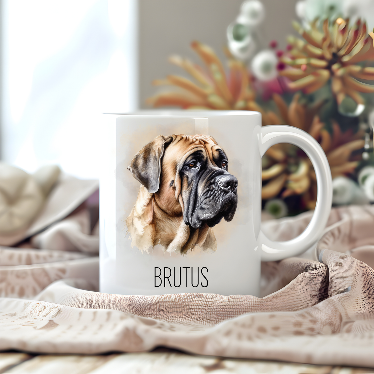 A white ceramic mug with a vibrant image of a Bullmastiff sits on a beige tablecloth placed on a wooden surface.  The mug is personalised with a pet name and stems of large flowers decorate the background.