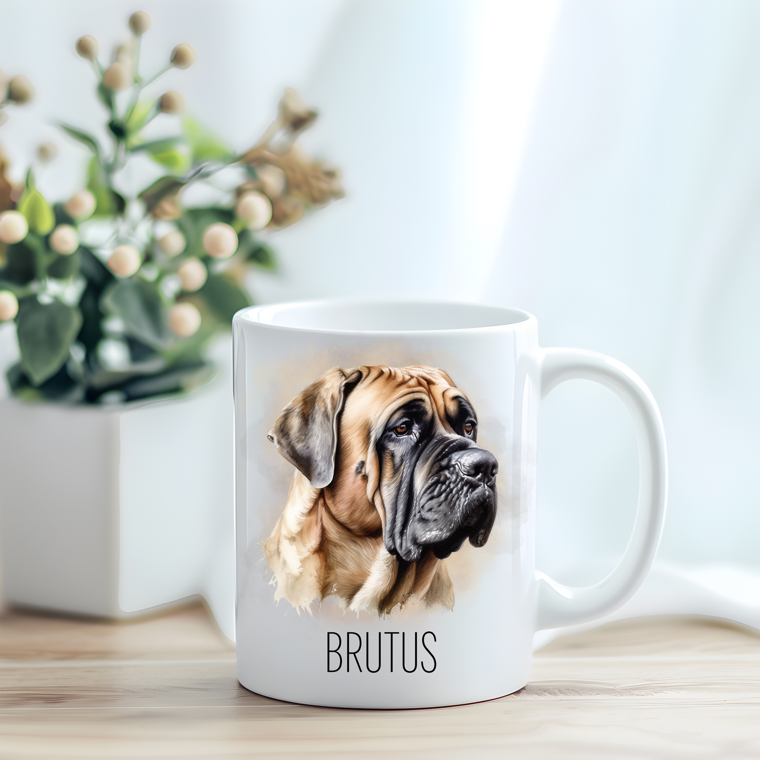 This coffee mug features a Bullmastiff on a white ceramic mug which has been placed on a light wooden surface.  A green and white plant sits on the left side of the image in a square plant pot.
