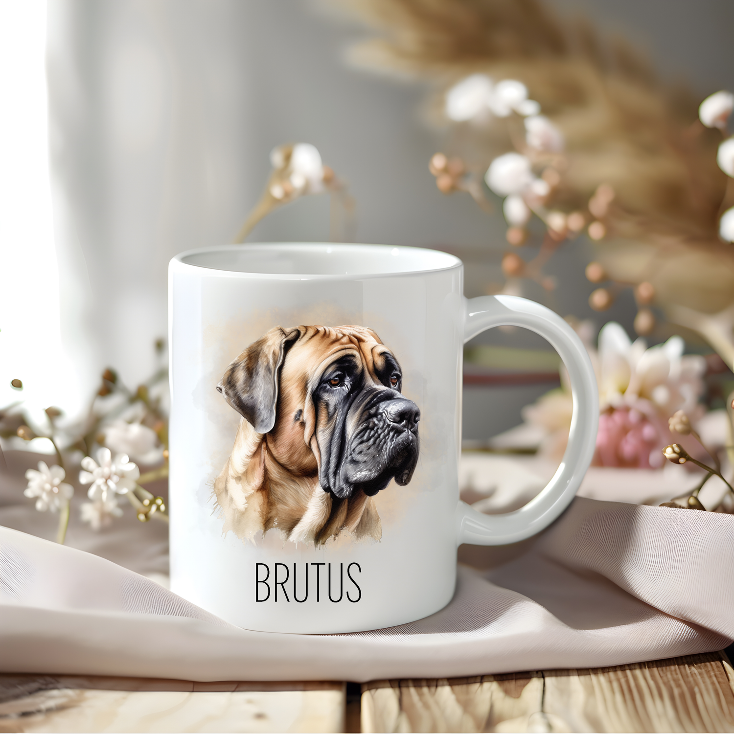 A lovely Bullmastiff coffee mug personalised with a pet name.  The mug is sat on a wooden surface with a creamy coloured cloth and a variety of flowers decorate the background.