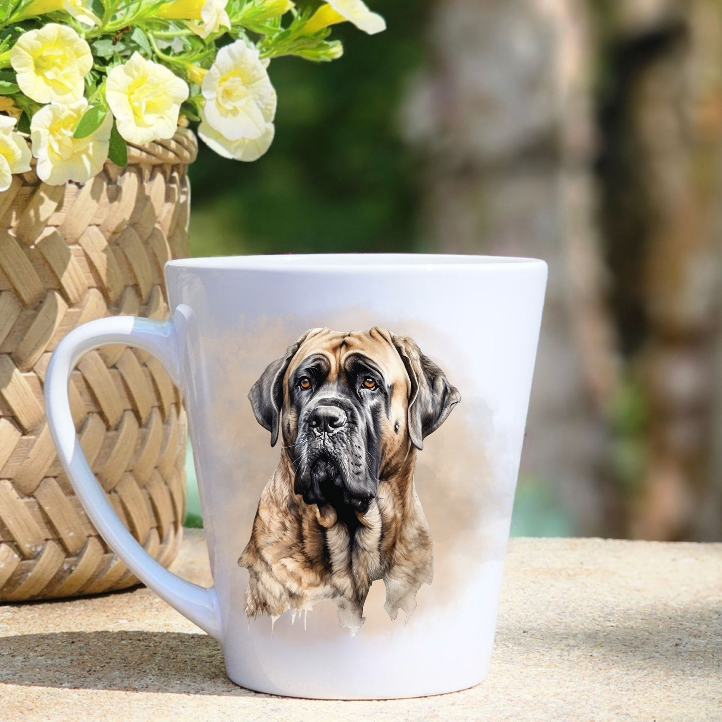 A white ceramic latte mug featuring a Bullmastiff headshot in a beige mist background.  A basket containing yellow flowers sits to the left-hand side.