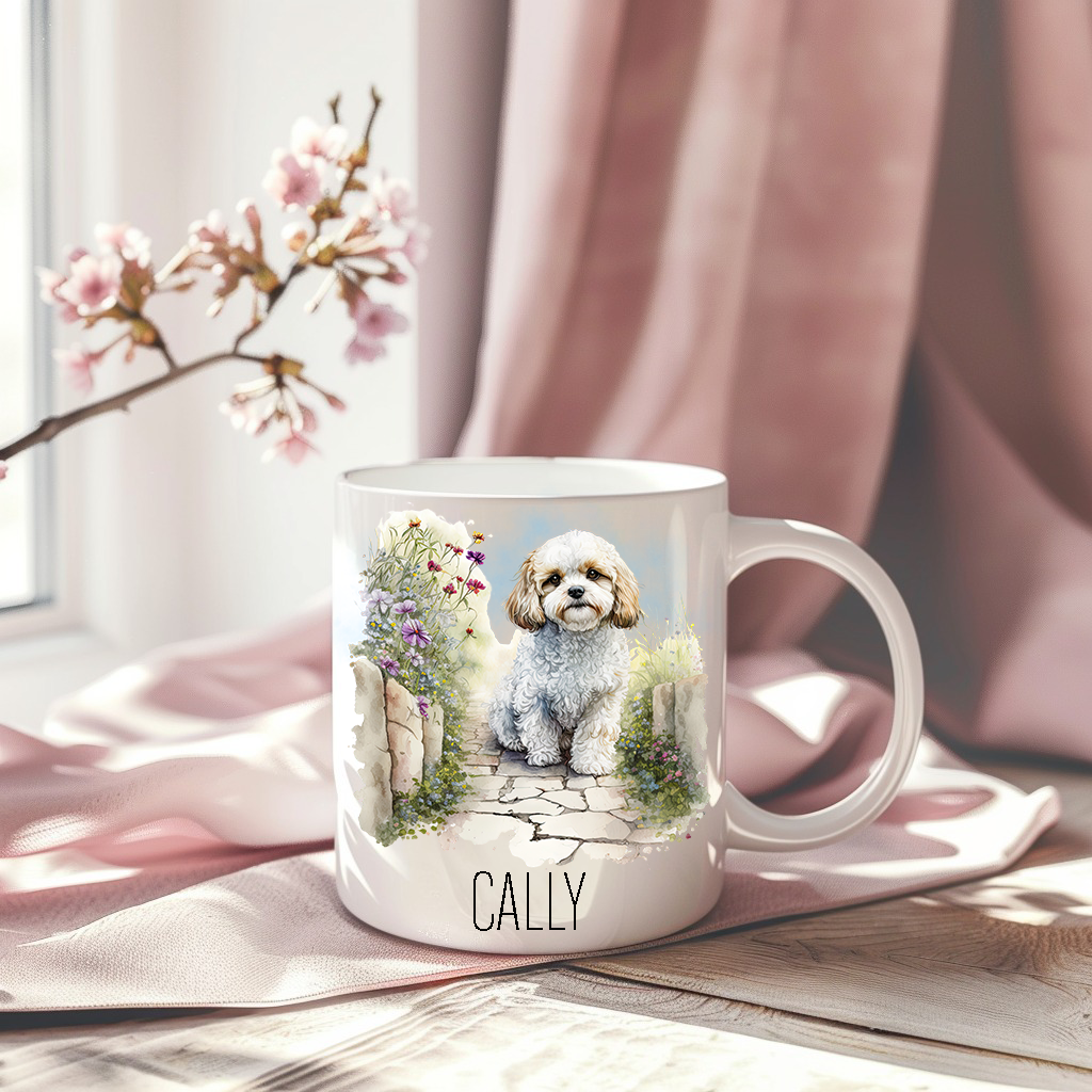 Cavachon in a sitting in a garden scene on a white ceramic mug which has been placed on a pink drape.  A stem of small pink flowers accessorizes the image.