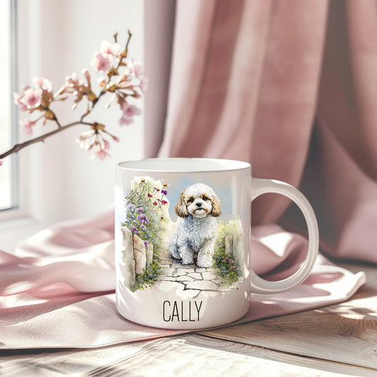 Cavachon in a sitting in a garden scene on a white ceramic mug which has been placed on a pink drape. A stem of small pink flowers accessorizes the image.