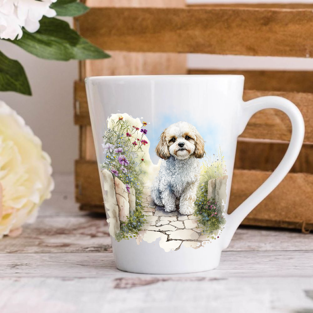A white ceramic latte mug stands on a wooden surface with a crate in the background. The mug features a Cavachon in a garden.  A large yellow flower peeps in from the left-hand side.