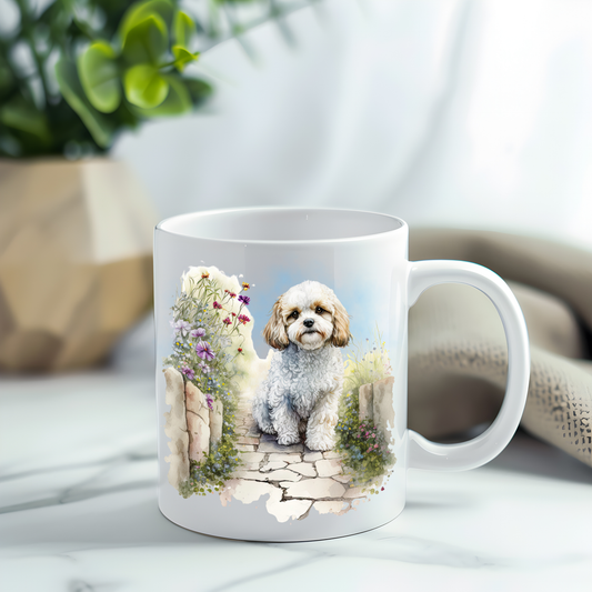 A Cavachon dog is in a sitting position on a crazy paved footpath among a garden scene on a white ceramic mug. The mug has been placed on a grey marble surface. A plant decorates the left corner.