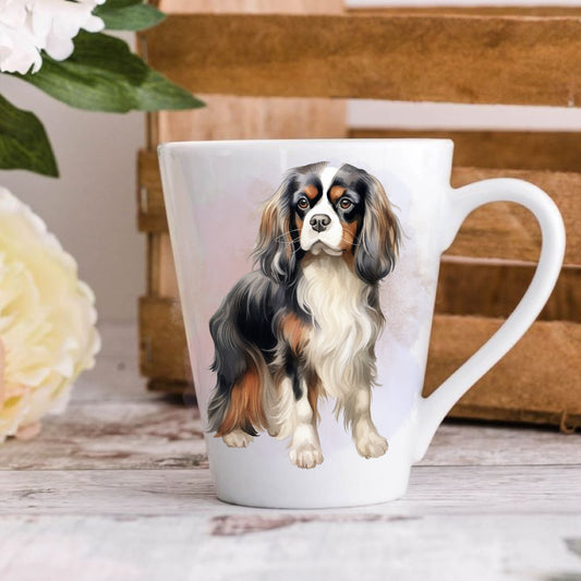 A ceramic latte coffee mug with a printed image of a Cavalier King Charles Spaniel on both sides, placed on a wooden surface with a floral pattern and books in the background.