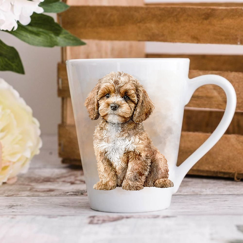 A white ceramic latte mug stands on a wooden surface with a crate in the background. The mug features a Cavapoo.  A large yellow flower peeps in from the left-hand side.