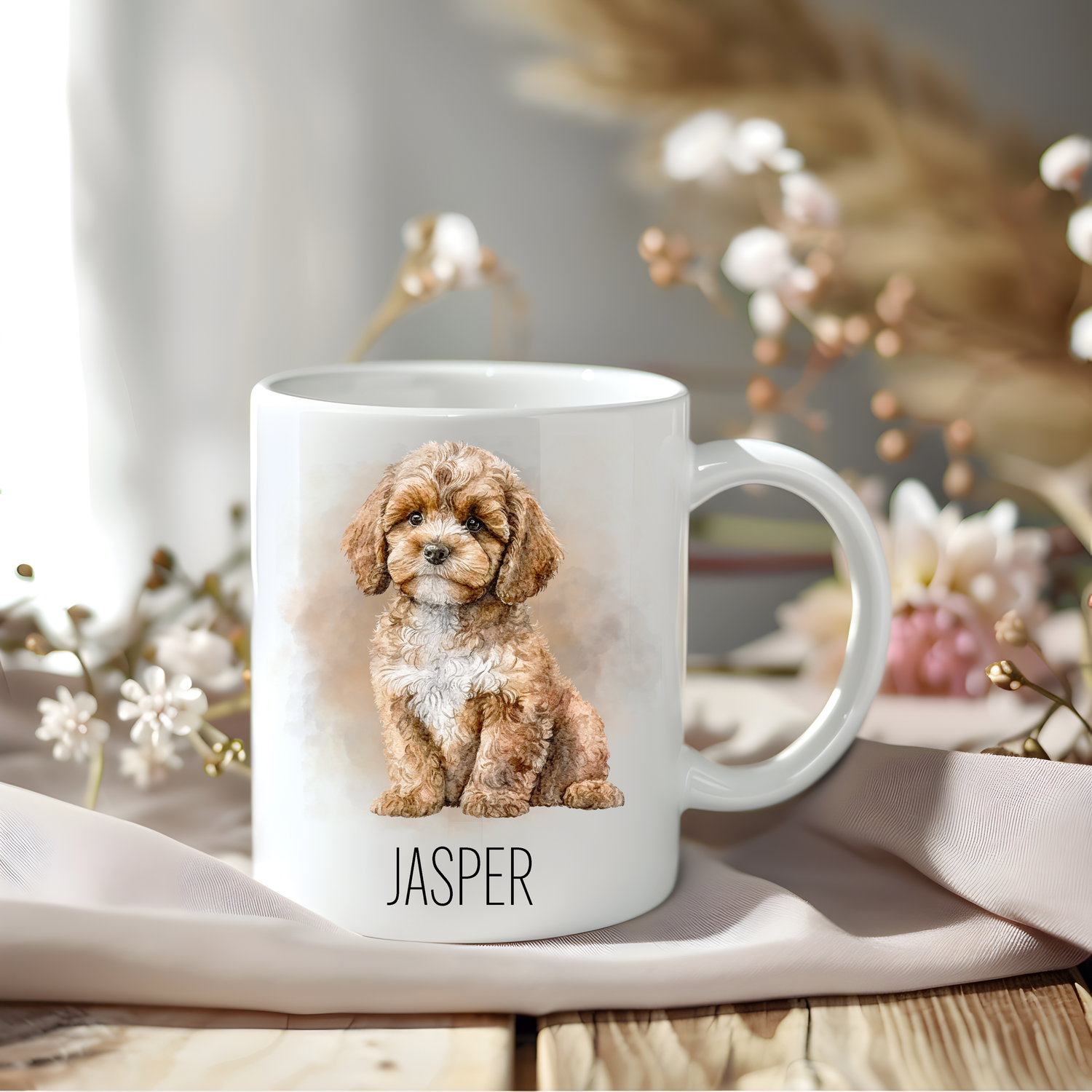 Cavapoo coffee mug personalised with a pet name.  The mug is sat on a wooden surface with a creamy coloured cloth and various flowers adorn the background.