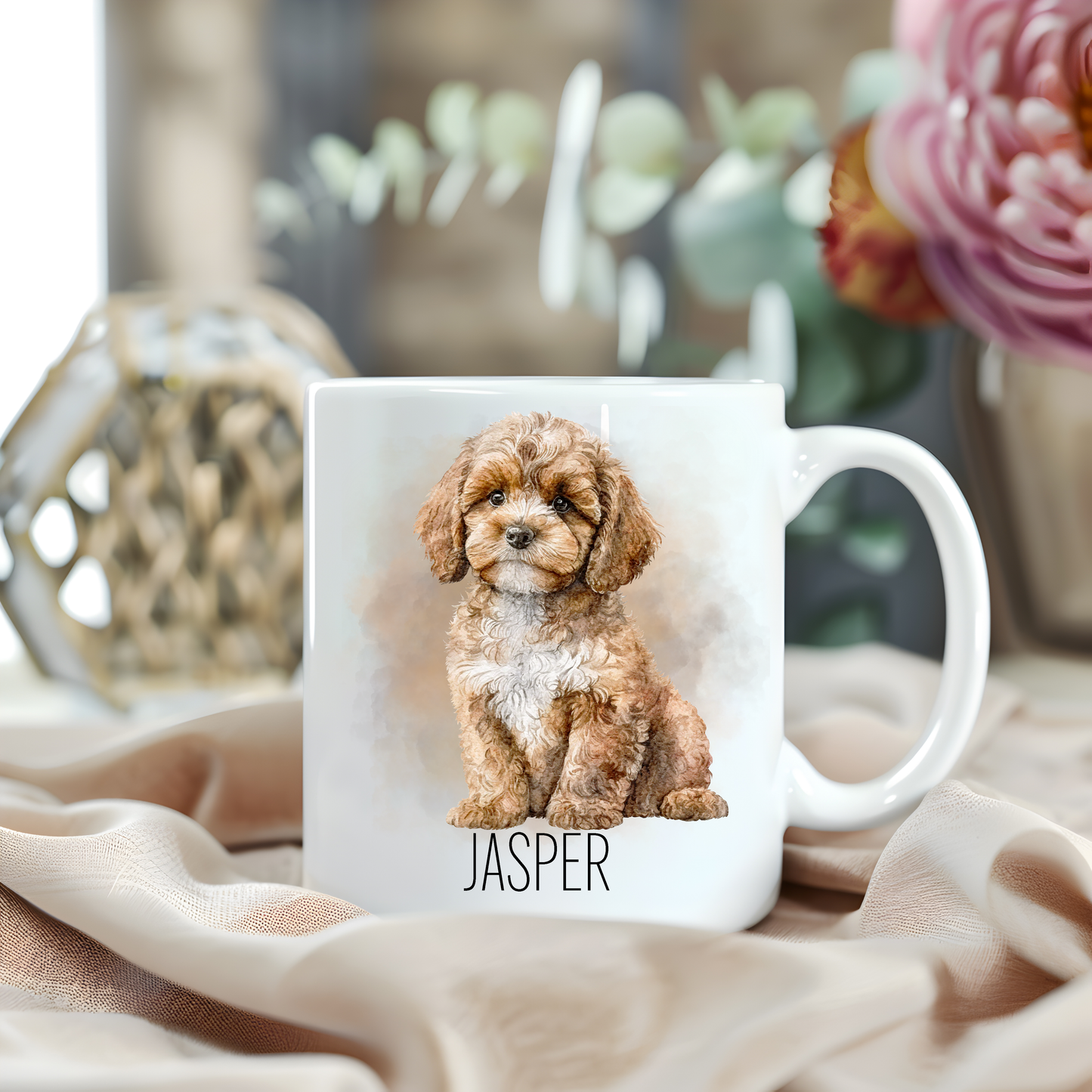 Personalised coffee mug featuring a seated Cavapoo dog on a white ceramic mug which has been placed on a beige cloth.  A large pink flower with green foliage accessorizes the image.
